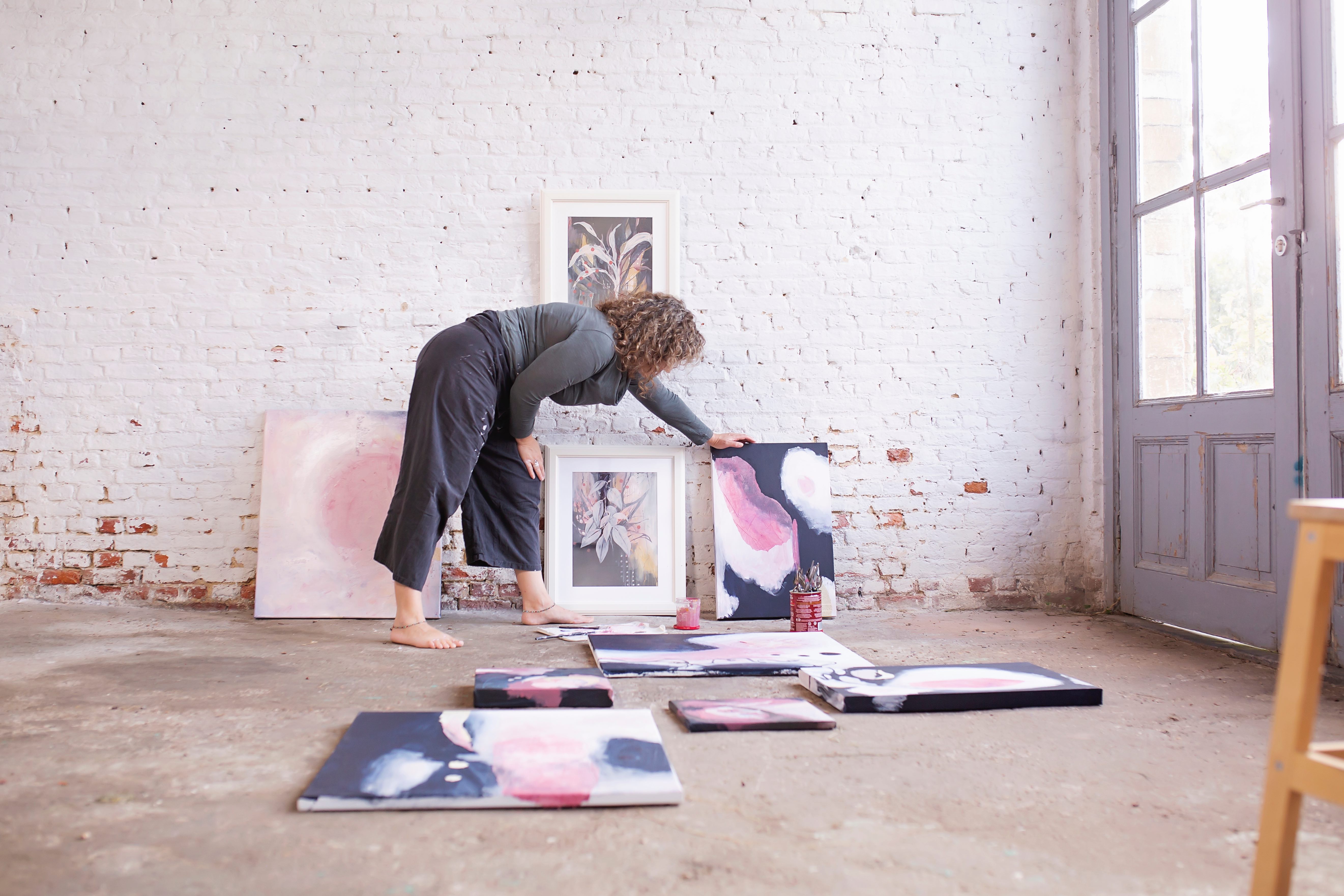 Mieke in her studio, barefoot and immersed in the creative process with her paintings