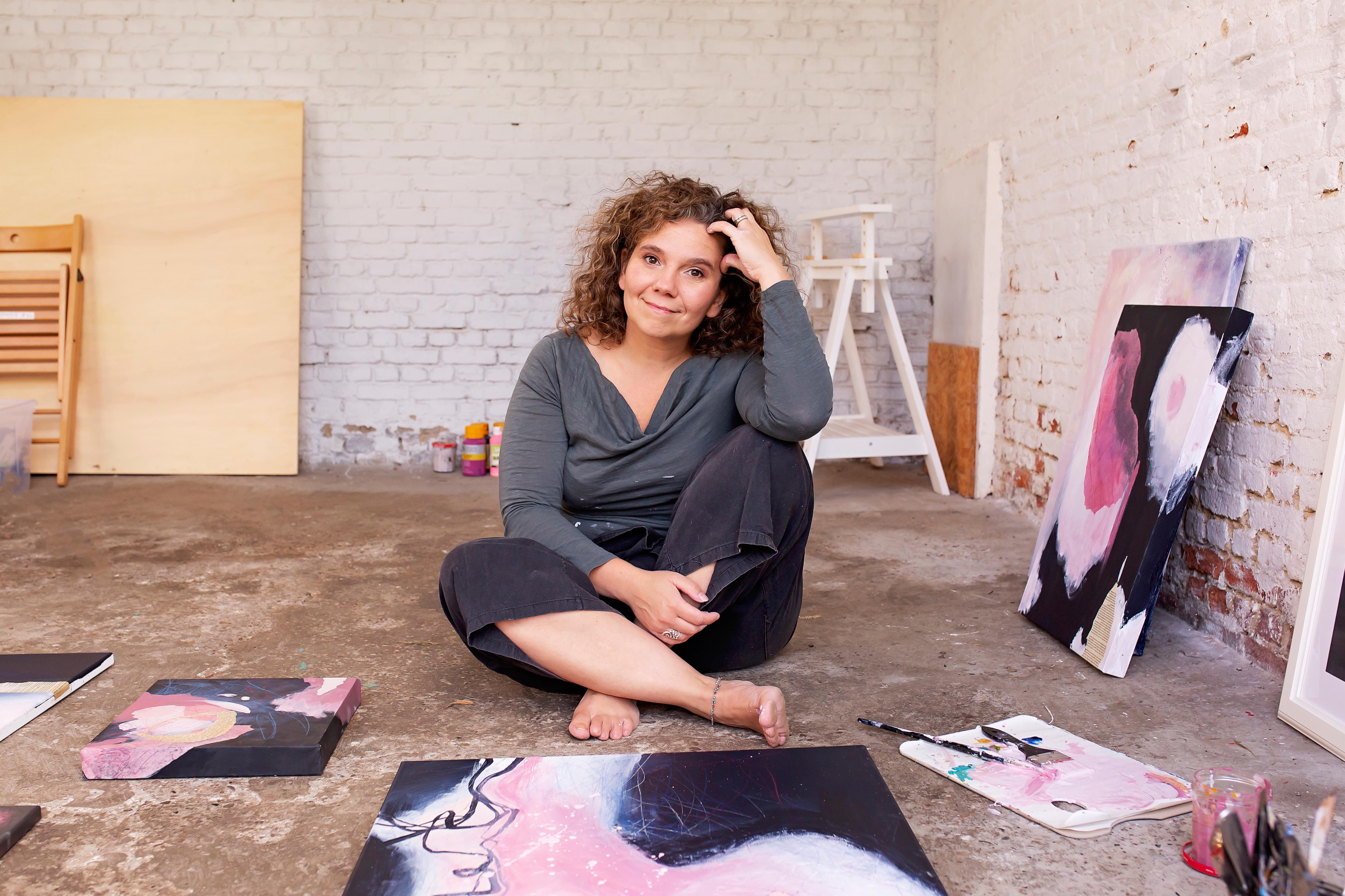 Mieke sitting on the floor of her studio surrounded by her paintings